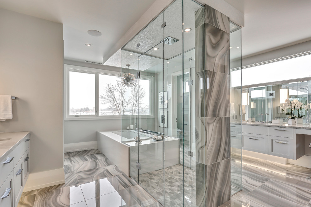 Photo of a contemporary master bathroom in Calgary with recessed-panel cabinets, beige cabinets, a freestanding tub, an open shower, gray tile, grey walls, an undermount sink, grey floor, a hinged shower door and beige benchtops.