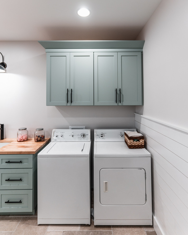 This is an example of a large country l-shaped dedicated laundry room in Other with shaker cabinets, blue cabinets, wood benchtops, white splashback, shiplap splashback, white walls, ceramic floors, a side-by-side washer and dryer, grey floor and brown benchtop.