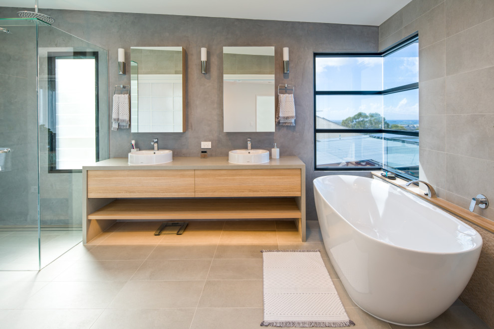 Photo of a large modern master bathroom in Sunshine Coast with flat-panel cabinets, beige cabinets, a freestanding tub, a curbless shower, a one-piece toilet, gray tile, cement tile, grey walls, cement tiles, a console sink, engineered quartz benchtops, grey floor, a hinged shower door and beige benchtops.