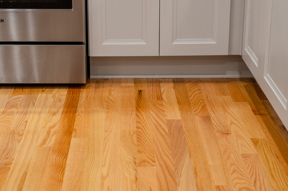 Example of a small transitional l-shaped medium tone wood floor and brown floor eat-in kitchen design with a double-bowl sink, shaker cabinets, gray cabinets, quartz countertops, white backsplash, subway tile backsplash, stainless steel appliances, no island and white countertops