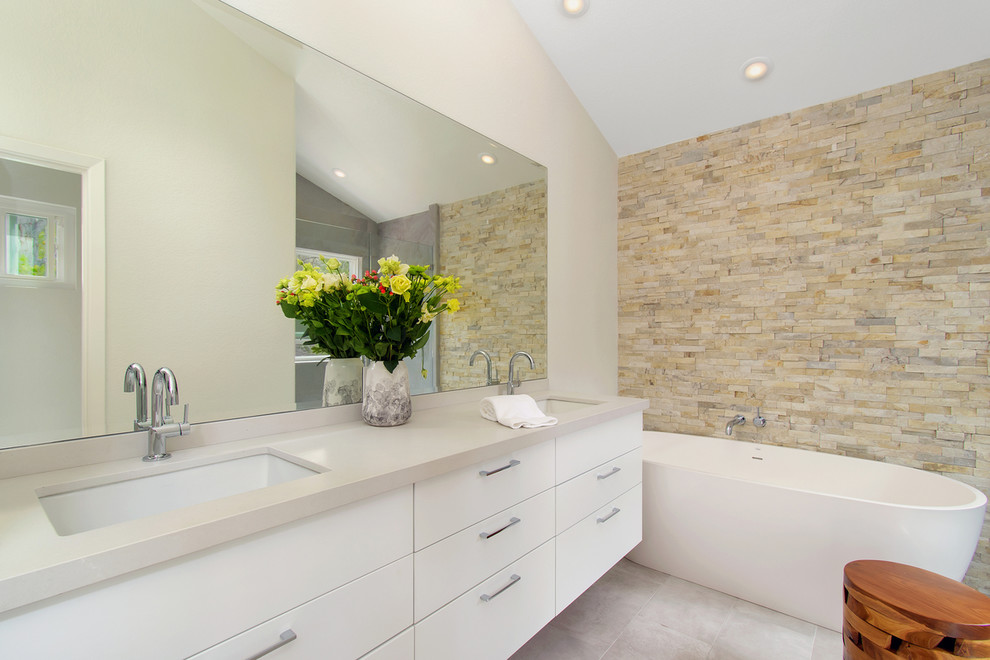 Inspiration for a mid-sized modern master bathroom in San Diego with flat-panel cabinets, white cabinets, a freestanding tub, an alcove shower, beige tile, white walls, porcelain floors, an undermount sink, engineered quartz benchtops, grey floor, a hinged shower door and grey benchtops.