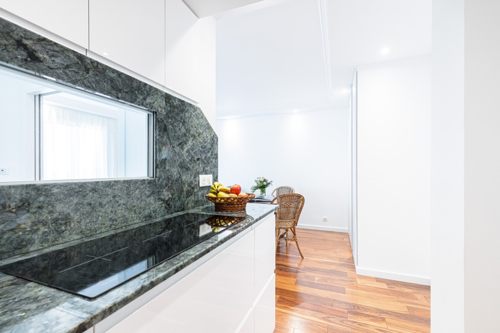 Photo of a small transitional single-wall open plan kitchen in Nice with an undermount sink, flat-panel cabinets, white cabinets, granite benchtops, blue splashback, granite splashback, panelled appliances, dark hardwood floors and blue benchtop.