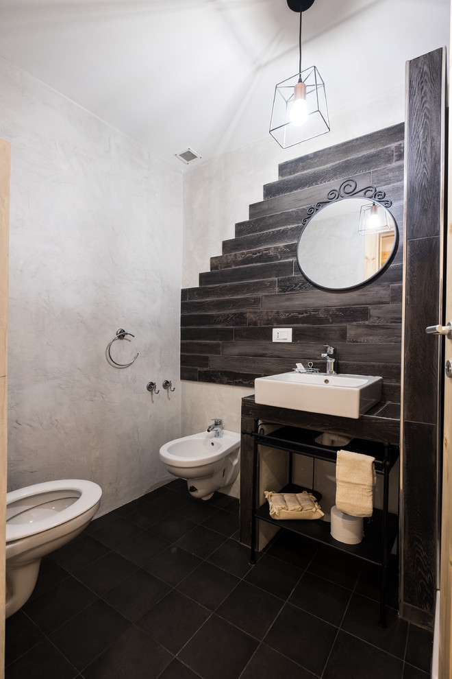 Design ideas for a mid-sized contemporary powder room in Other with open cabinets, brown cabinets, a wall-mount toilet, brown tile, porcelain tile, grey walls, porcelain floors, a vessel sink, solid surface benchtops, black floor and brown benchtops.
