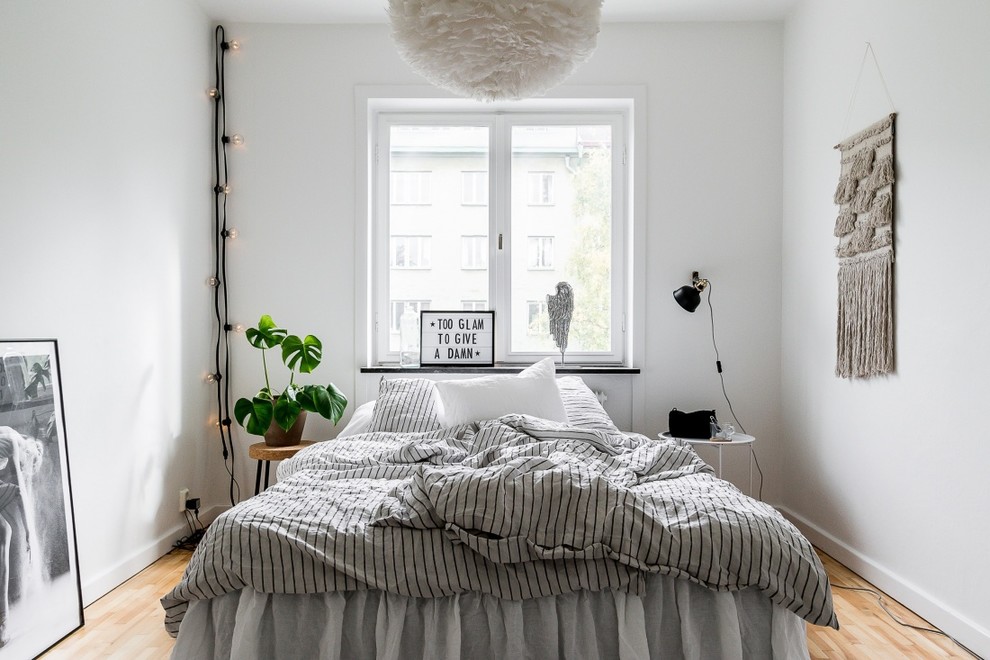 This is an example of a small scandinavian bedroom in Stockholm with white walls, light hardwood floors and beige floor.
