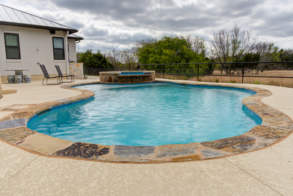 Large transitional backyard stamped concrete and kidney-shaped lap hot tub photo in Austin