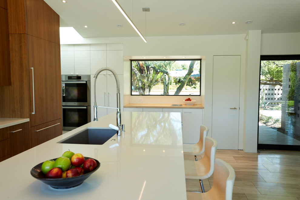 Design ideas for a mid-sized modern galley open plan kitchen in Phoenix with an undermount sink, flat-panel cabinets, medium wood cabinets, quartz benchtops, blue splashback, glass tile splashback, panelled appliances, limestone floors and with island.