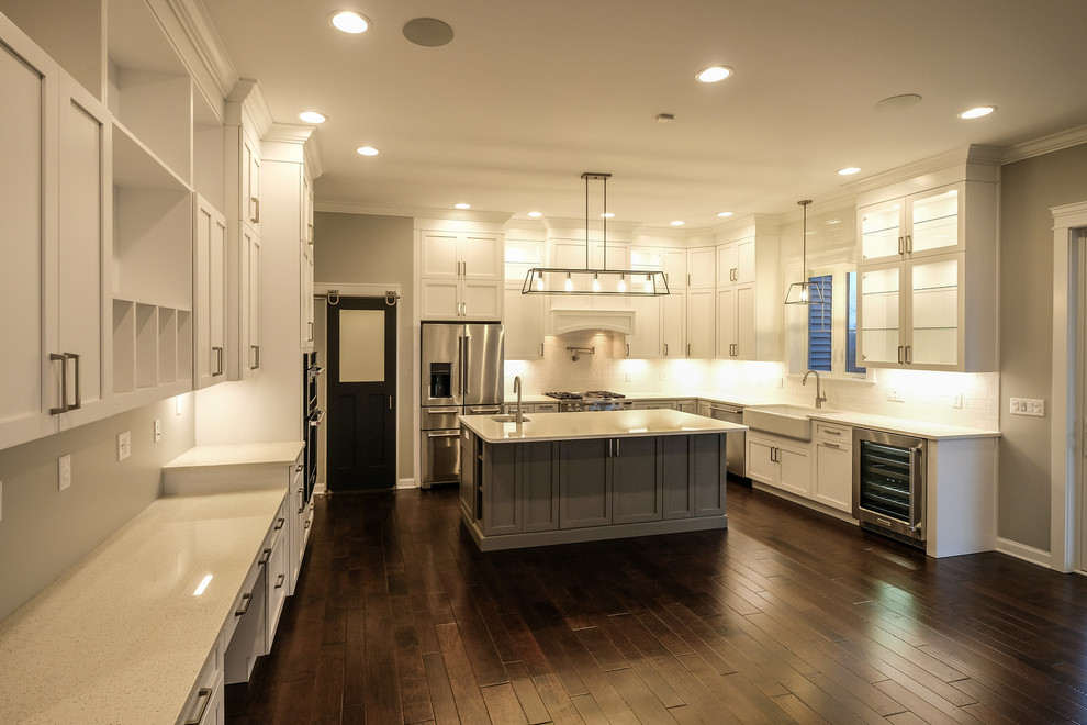 Example of a large transitional u-shaped dark wood floor and brown floor eat-in kitchen design with a farmhouse sink, recessed-panel cabinets, white cabinets, quartz countertops, white backsplash, stainless steel appliances, an island and white countertops