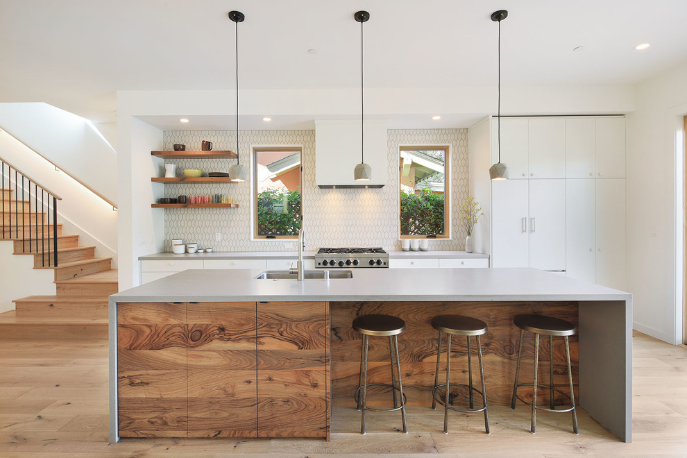 This is an example of a contemporary galley kitchen in San Francisco with an undermount sink, flat-panel cabinets, white cabinets, stainless steel appliances, medium hardwood floors, with island, brown floor and white benchtop.