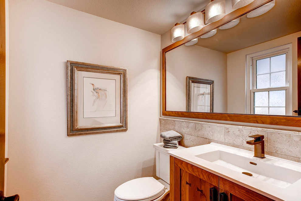 This is an example of a small arts and crafts powder room in Denver with an integrated sink, shaker cabinets, medium wood cabinets, solid surface benchtops, a two-piece toilet, beige tile, ceramic tile and beige walls.