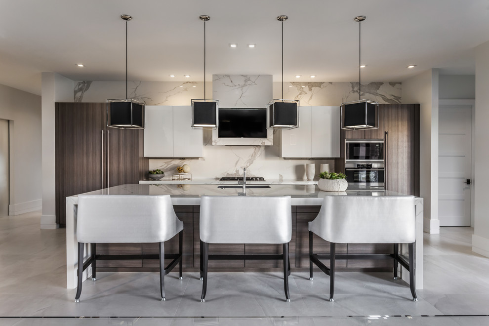 Large contemporary kitchen in Miami with flat-panel cabinets, marble benchtops, white splashback, marble splashback, stainless steel appliances, ceramic floors, with island, white benchtop, an undermount sink, white cabinets and grey floor.