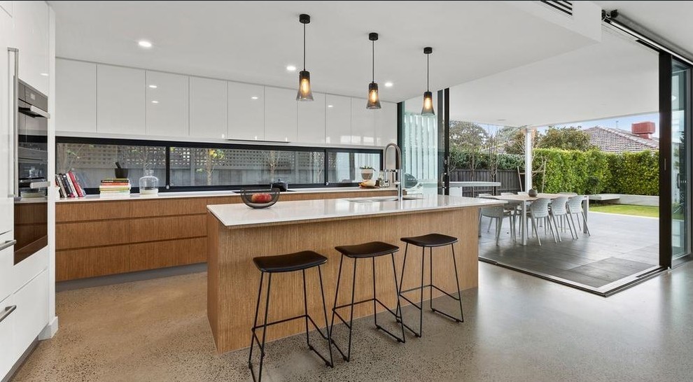 Photo of a contemporary galley open plan kitchen in Melbourne with flat-panel cabinets, medium wood cabinets, window splashback, concrete floors, with island, grey floor and white benchtop.