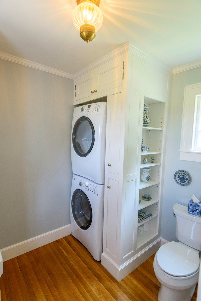 Inspiration for a timeless medium tone wood floor utility room remodel in Burlington with white cabinets and a stacked washer/dryer