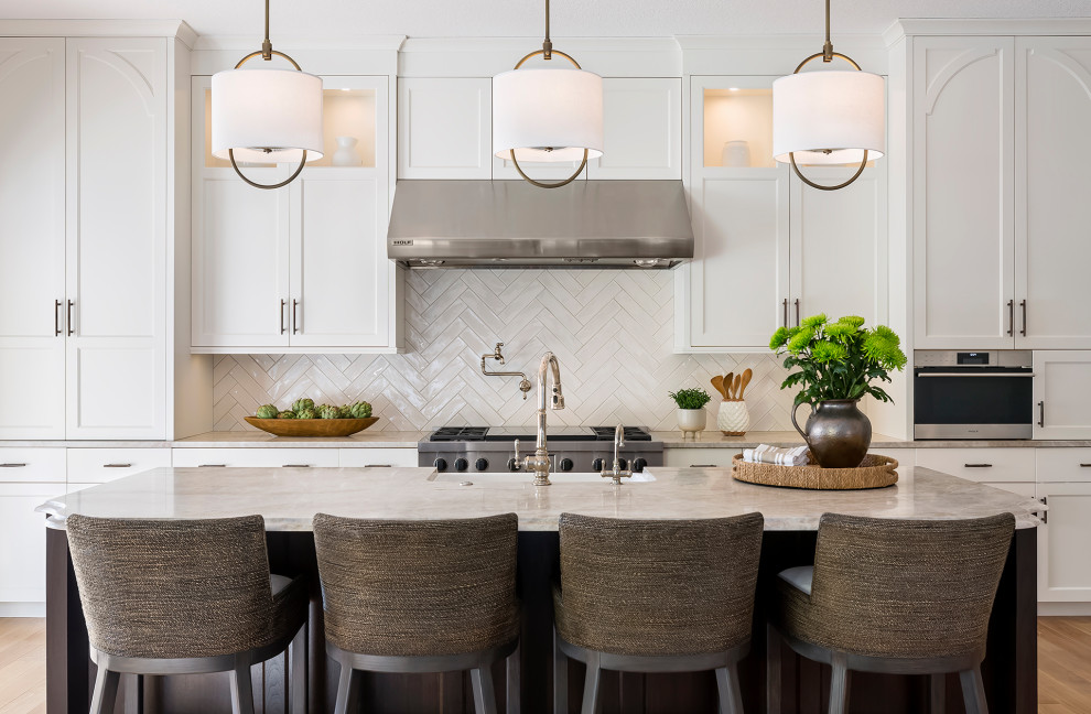 Open concept kitchen - large transitional single-wall light wood floor and brown floor open concept kitchen idea in Minneapolis with a farmhouse sink, recessed-panel cabinets, white cabinets, quartzite countertops, white backsplash, ceramic backsplash, stainless steel appliances, an island and beige countertops