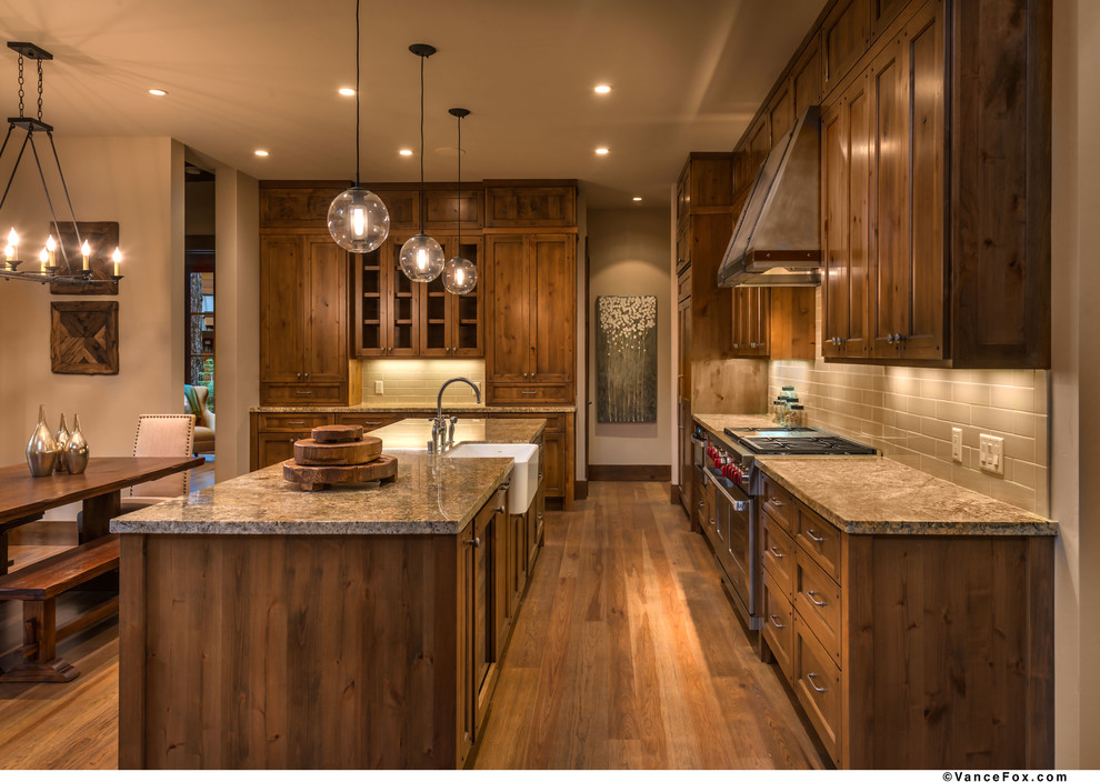 This is an example of a mid-sized country l-shaped eat-in kitchen in Sacramento with a farmhouse sink, shaker cabinets, medium wood cabinets, granite benchtops, beige splashback, subway tile splashback, panelled appliances, medium hardwood floors and with island.