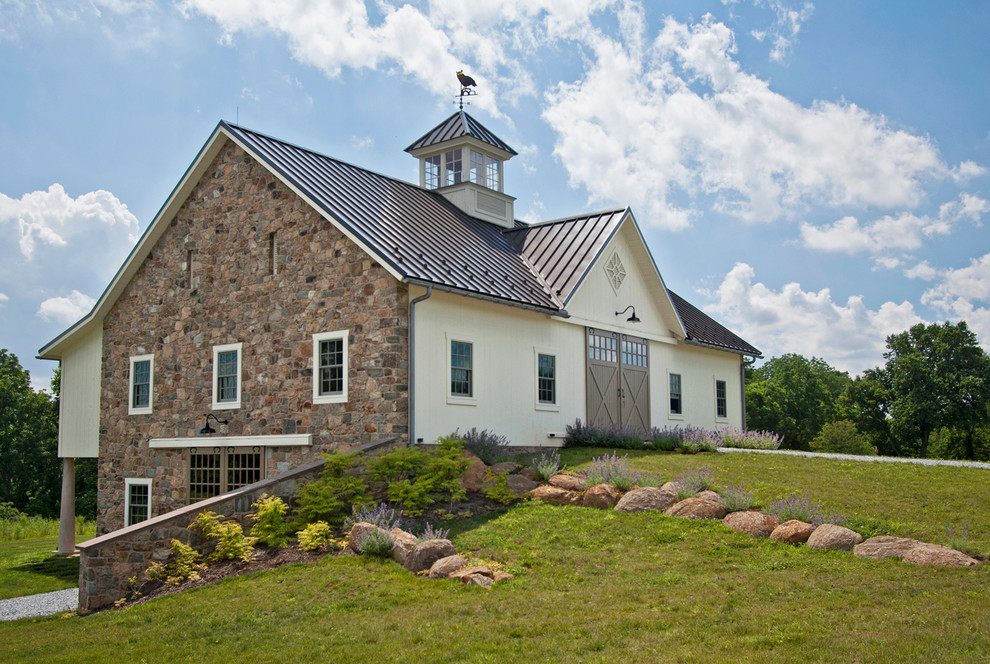 Example of a mid-sized farmhouse beige two-story stone gable roof design in Philadelphia with a metal roof