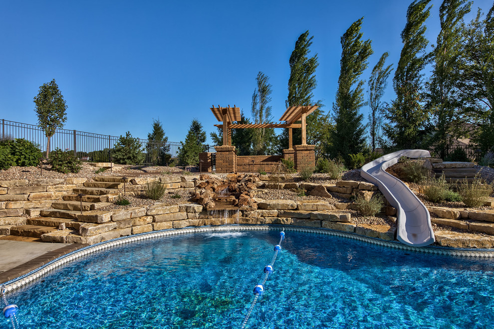 Large mountain style backyard concrete paver and custom-shaped pool fountain photo in Omaha