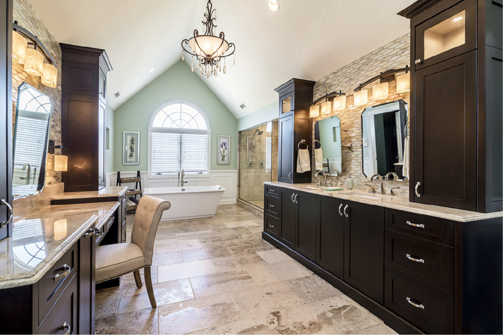 This is an example of an expansive transitional master bathroom in Chicago with shaker cabinets, dark wood cabinets, a freestanding tub, a double shower, a two-piece toilet, beige tile, glass sheet wall, green walls, travertine floors, an undermount sink and granite benchtops.