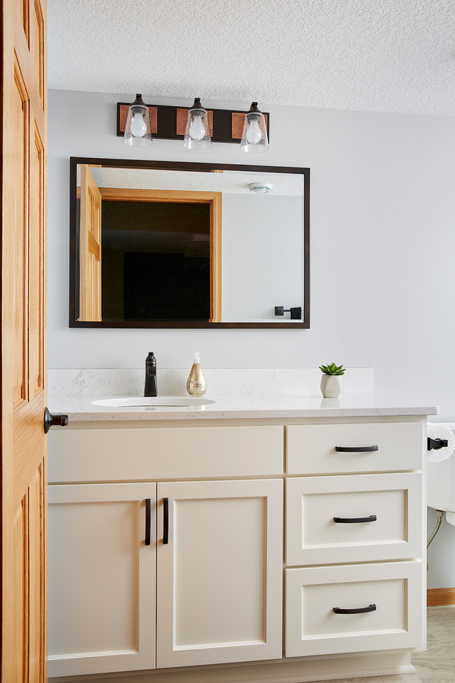 Inspiration for a mid-sized transitional powder room in Minneapolis with recessed-panel cabinets, white cabinets, white walls, an undermount sink, beige floor and white benchtops.