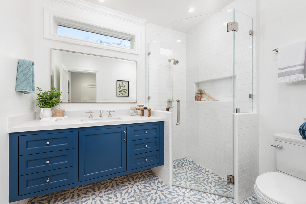 Inspiration for a mid-sized country 3/4 bathroom in San Francisco with blue cabinets, a corner shower, white tile, ceramic tile, white walls, ceramic floors, an undermount sink, engineered quartz benchtops, blue floor, a hinged shower door, white benchtops, recessed-panel cabinets and a two-piece toilet.