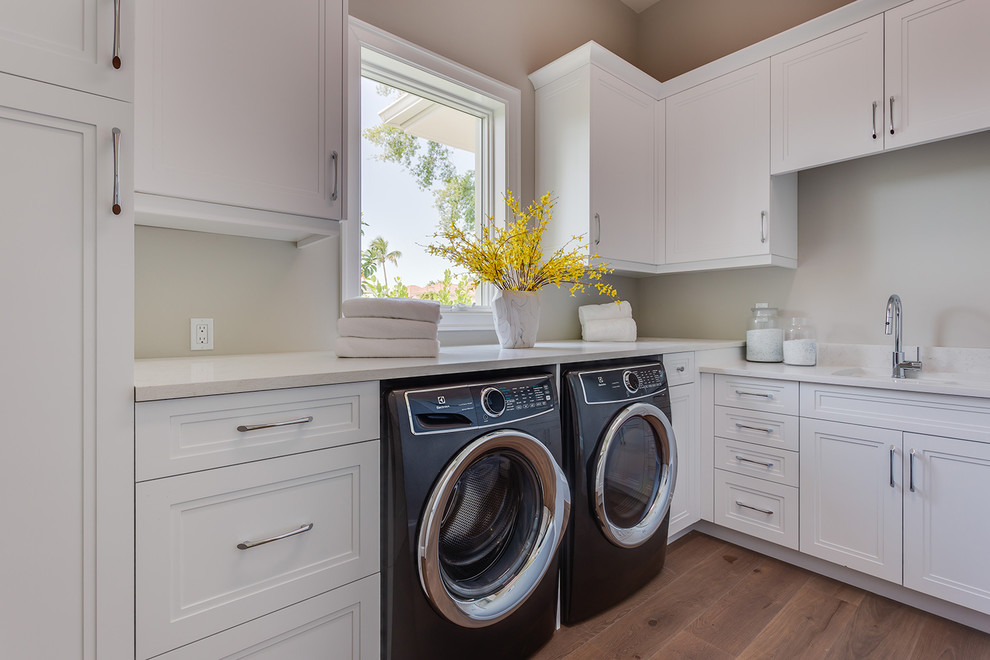 Photo of a mid-sized contemporary l-shaped dedicated laundry room in Other with recessed-panel cabinets, white cabinets, granite benchtops, grey walls, light hardwood floors, a side-by-side washer and dryer, beige floor and beige benchtop.