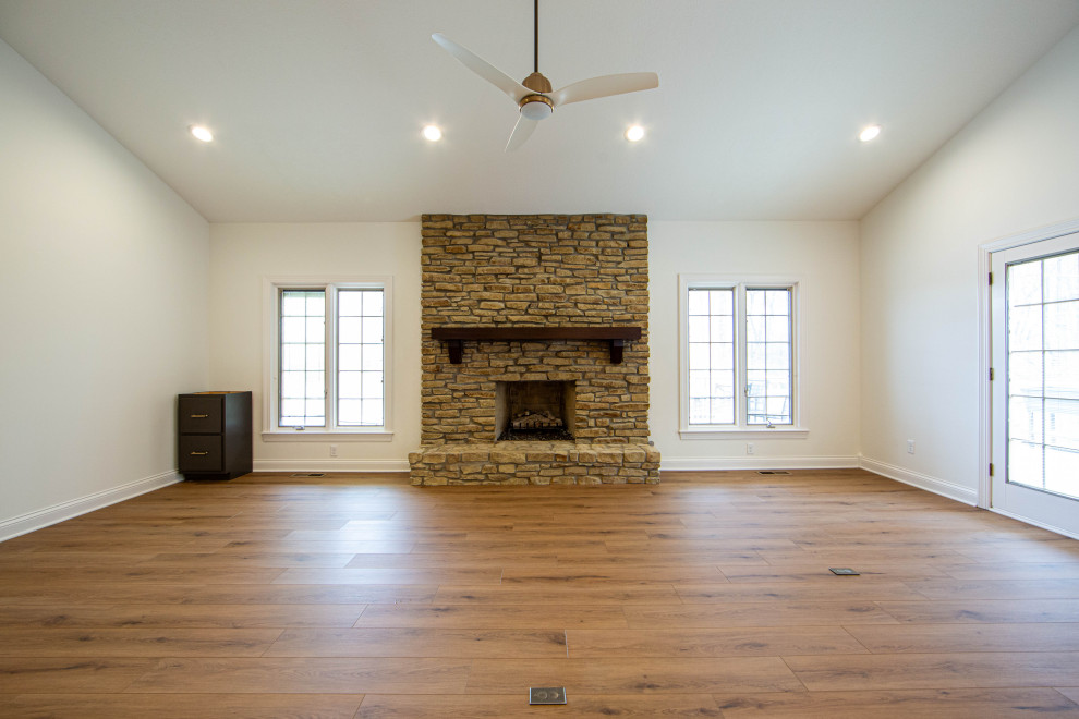 Photo of a medium sized traditional open plan living room in Indianapolis with beige walls, laminate floors, a standard fireplace, a stone fireplace surround, brown floors and a vaulted ceiling.
