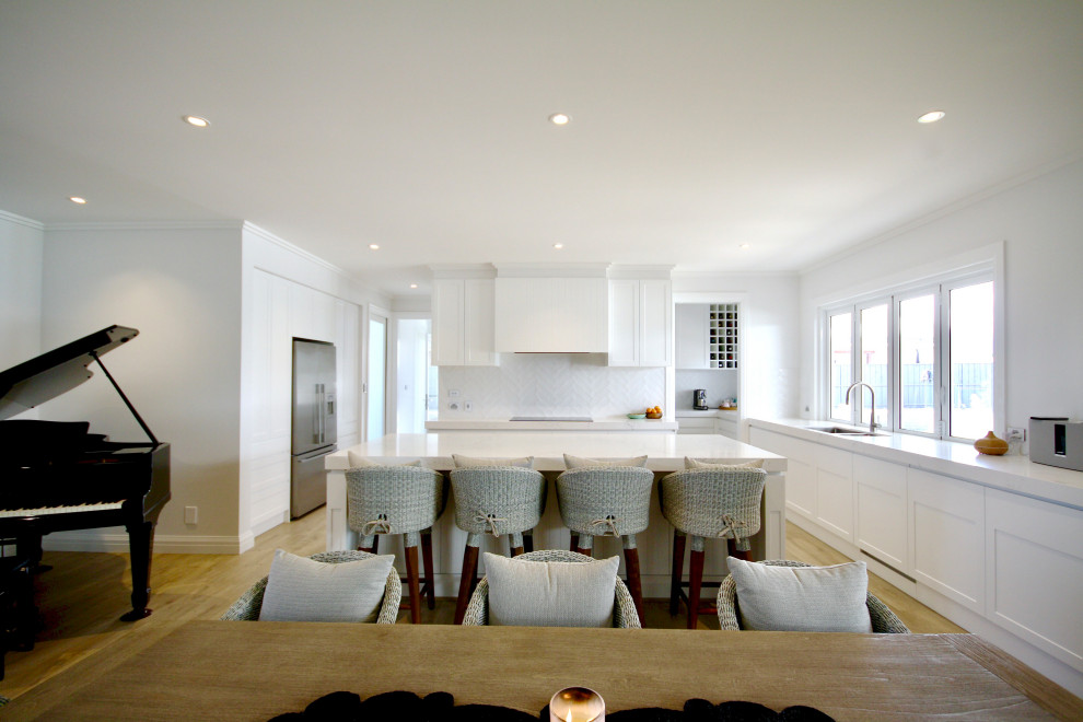 Design ideas for an expansive transitional u-shaped open plan kitchen in Sydney with an undermount sink, shaker cabinets, white cabinets, quartz benchtops, white splashback, subway tile splashback, stainless steel appliances, medium hardwood floors, with island, brown floor, white benchtop and recessed.