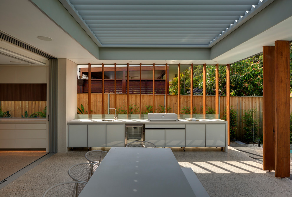 This is an example of a mid-sized contemporary backyard patio in Sydney with an outdoor kitchen, concrete slab and a pergola.