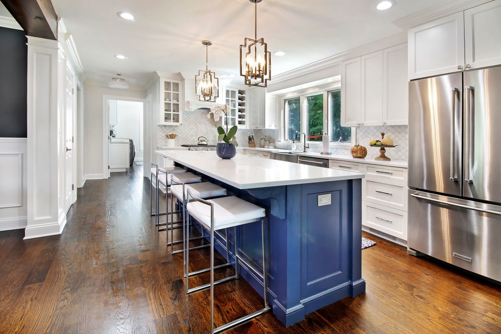 Design ideas for a transitional l-shaped kitchen in Grand Rapids with a farmhouse sink, recessed-panel cabinets, blue cabinets, white splashback, stainless steel appliances, dark hardwood floors, with island, brown floor and white benchtop.