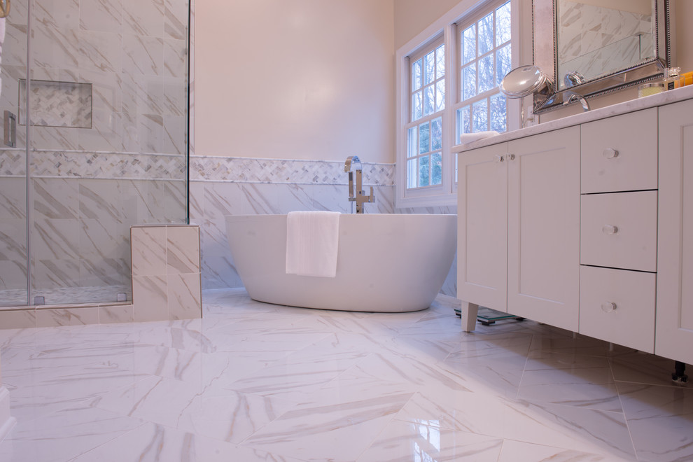 This is an example of a large contemporary master bathroom in DC Metro with furniture-like cabinets, white cabinets, a freestanding tub, a corner shower, marble and a hinged shower door.