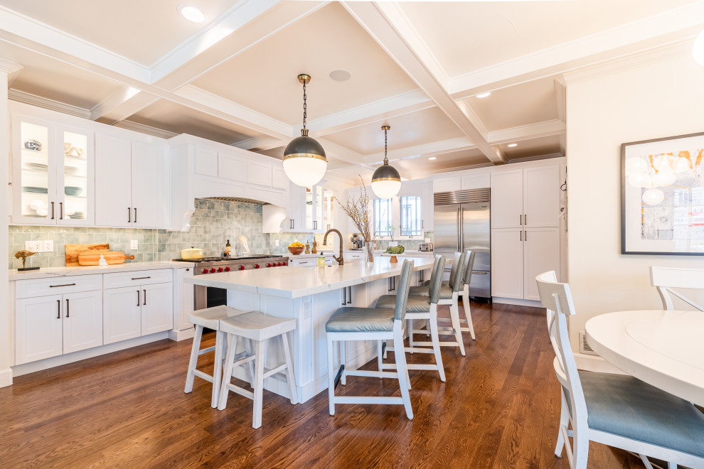 Photo of an expansive beach style l-shaped eat-in kitchen in Denver with a farmhouse sink, shaker cabinets, white cabinets, quartzite benchtops, multi-coloured splashback, ceramic splashback, stainless steel appliances, medium hardwood floors, with island, white benchtop and exposed beam.