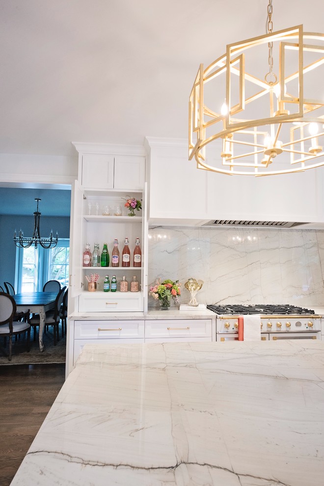 Example of a large transitional l-shaped medium tone wood floor and brown floor open concept kitchen design with a farmhouse sink, recessed-panel cabinets, white cabinets, quartzite countertops, white backsplash, stone slab backsplash, paneled appliances and an island