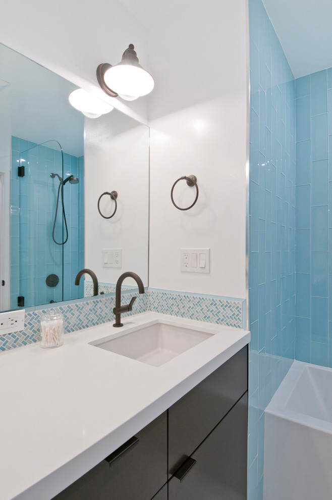 This is an example of a large contemporary kids bathroom in Los Angeles with flat-panel cabinets, brown cabinets, an alcove tub, a shower/bathtub combo, blue tile, glass tile, white walls, porcelain floors, an undermount sink, solid surface benchtops, white floor and white benchtops.