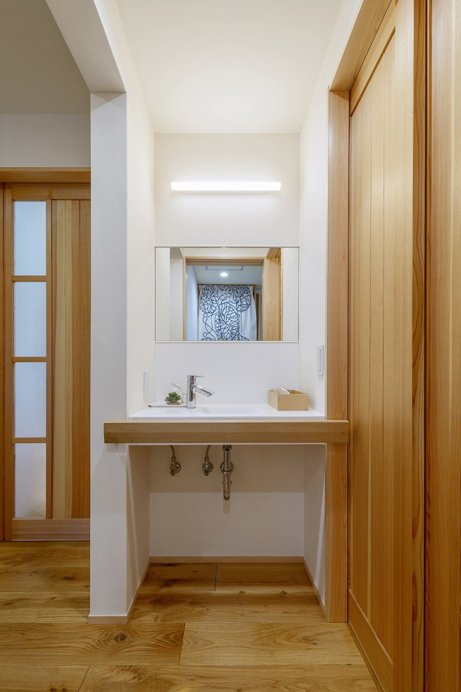 Inredning av ett modernt mellanstort vit vitt toalett, med öppna hyllor, vita skåp, en toalettstol med hel cisternkåpa, vita väggar, mellanmörkt trägolv, ett väggmonterat handfat, bänkskiva i akrylsten och brunt golv