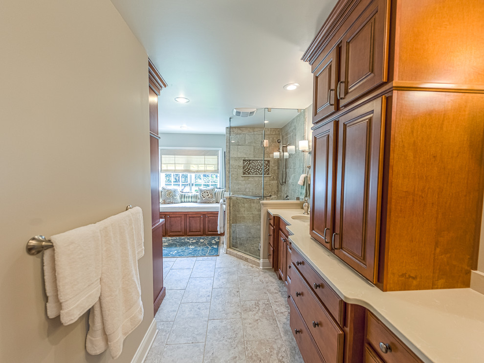 Example of a mid-sized transitional master beige tile and glass tile porcelain tile corner shower design with an undermount sink, raised-panel cabinets, medium tone wood cabinets, quartz countertops, a two-piece toilet and beige walls
