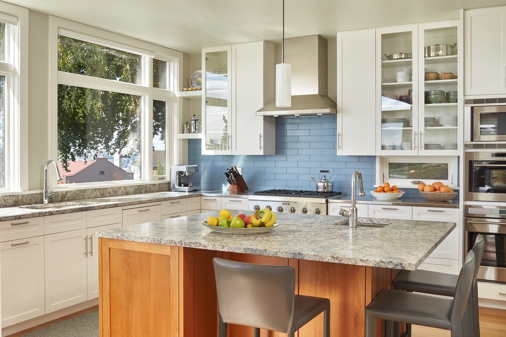 This is an example of a mid-sized transitional l-shaped separate kitchen in Seattle with an undermount sink, flat-panel cabinets, white cabinets, granite benchtops, blue splashback, glass tile splashback, stainless steel appliances, light hardwood floors and with island.