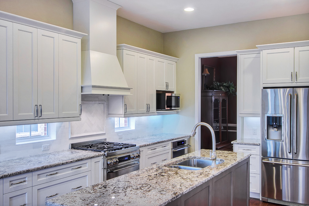 This is an example of a large transitional galley open plan kitchen in Dallas with an undermount sink, shaker cabinets, white cabinets, granite benchtops, white splashback, subway tile splashback, stainless steel appliances, medium hardwood floors and multiple islands.