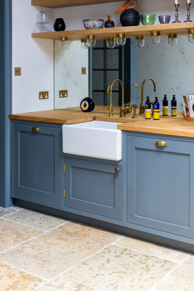 Inspiration for a large contemporary single-wall open plan kitchen in Wiltshire with a belfast sink, shaker cabinets, blue cabinets, wood worktops, metallic splashback, mirror splashback, limestone flooring, an island, brown floors and brown worktops.