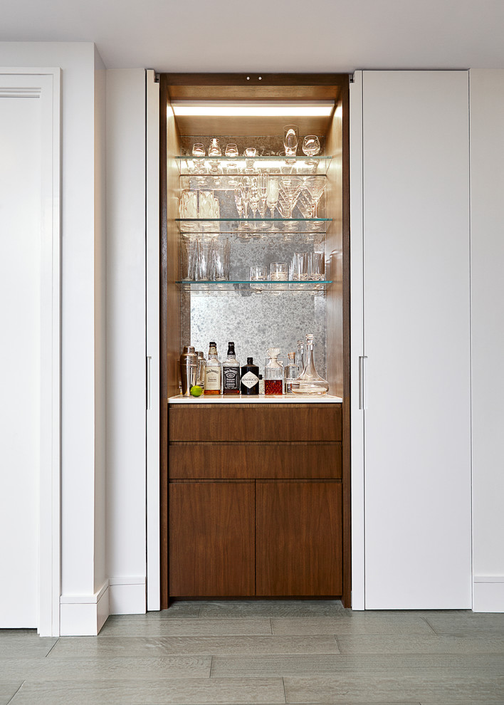 Photo of a small contemporary single-wall home bar in New York with flat-panel cabinets, quartz benchtops, mirror splashback, no sink, light hardwood floors, grey floor and medium wood cabinets.