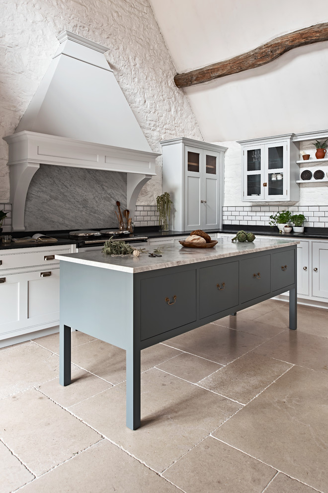 Photo of a large country l-shaped kitchen in Wiltshire with recessed-panel cabinets, white cabinets, marble benchtops, grey splashback, marble splashback, travertine floors, with island and beige floor.