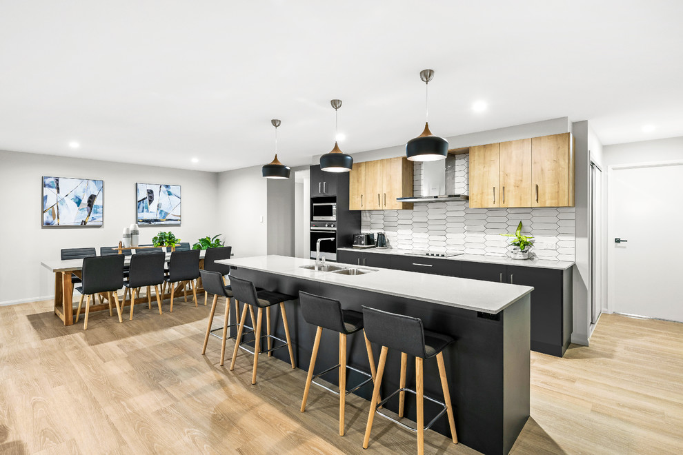 Photo of a contemporary galley eat-in kitchen in Other with a double-bowl sink, flat-panel cabinets, black cabinets, white splashback, stainless steel appliances, light hardwood floors, with island, brown floor and white benchtop.