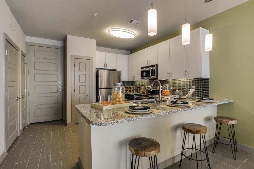 Inspiration for a mid-sized transitional l-shaped porcelain tile and gray floor open concept kitchen remodel in Houston with a double-bowl sink, flat-panel cabinets, black cabinets, granite countertops, black backsplash, mosaic tile backsplash, stainless steel appliances and a peninsula