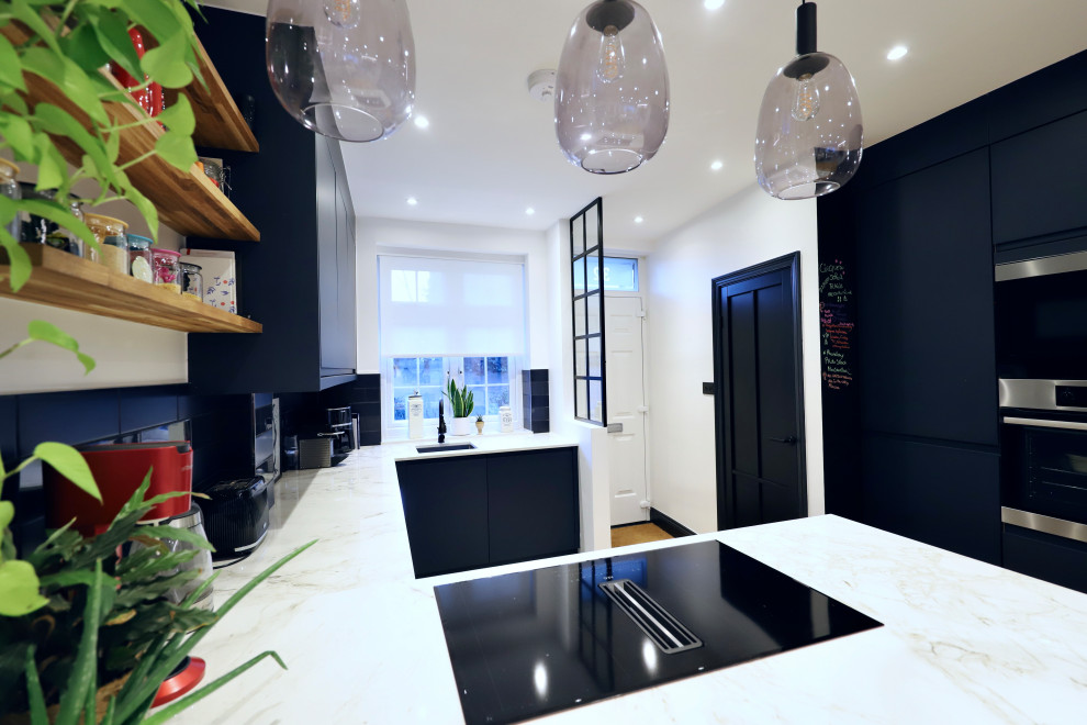 Photo of a medium sized contemporary u-shaped open plan kitchen in London with a built-in sink, flat-panel cabinets, blue cabinets, granite worktops, blue splashback, ceramic splashback, black appliances, light hardwood flooring, an island, white worktops and a feature wall.