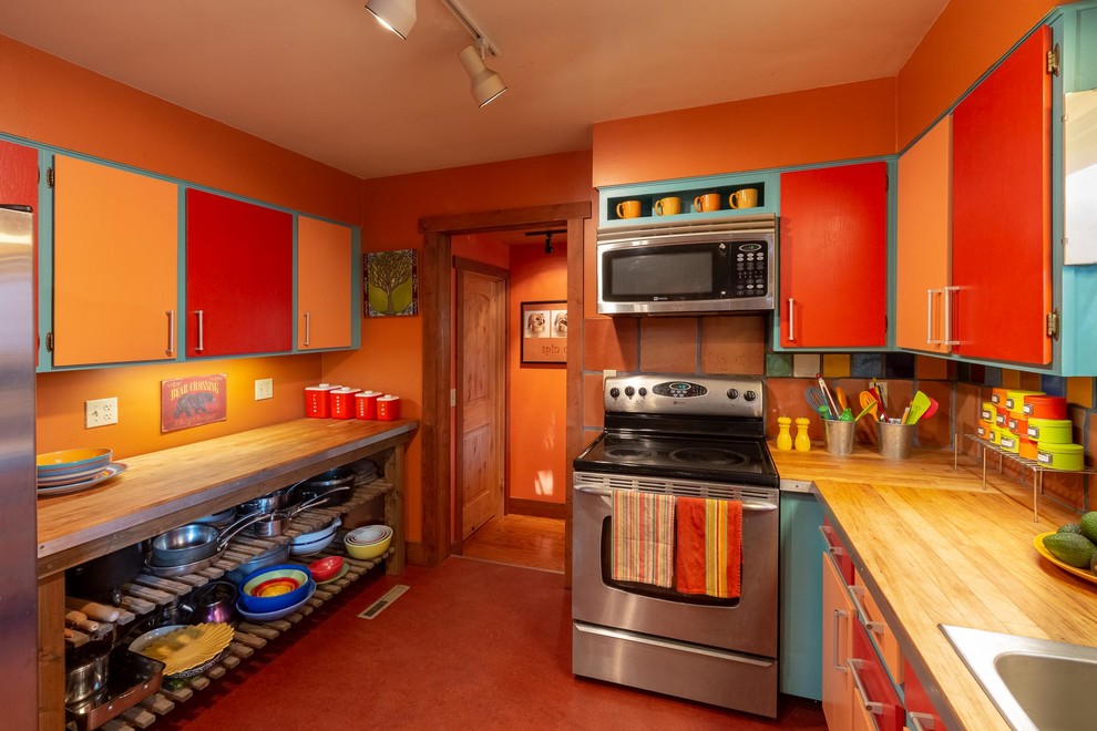 This is an example of a kitchen in Other with a drop-in sink, flat-panel cabinets, orange cabinets, wood benchtops, multi-coloured splashback, terra-cotta splashback, stainless steel appliances, linoleum floors, red floor and brown benchtop.