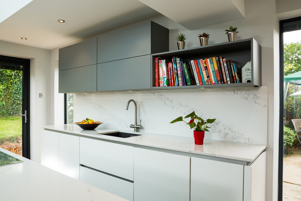 Large single-wall eat-in kitchen in Hampshire with an integrated sink, quartz benchtops, stainless steel appliances, with island, flat-panel cabinets, grey cabinets, white splashback, stone slab splashback and medium hardwood floors.
