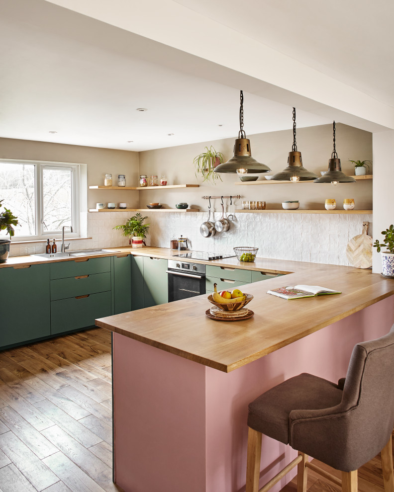 Design ideas for a mid-sized contemporary u-shaped open plan kitchen in Devon with flat-panel cabinets, green cabinets, wood benchtops, white splashback, stone tile splashback, medium hardwood floors, a peninsula, a drop-in sink, stainless steel appliances, brown floor and brown benchtop.
