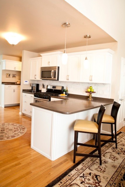 Example of a mid-sized transitional u-shaped light wood floor eat-in kitchen design in Charlotte with white cabinets, white backsplash, stainless steel appliances, a peninsula, shaker cabinets, solid surface countertops and stone tile backsplash