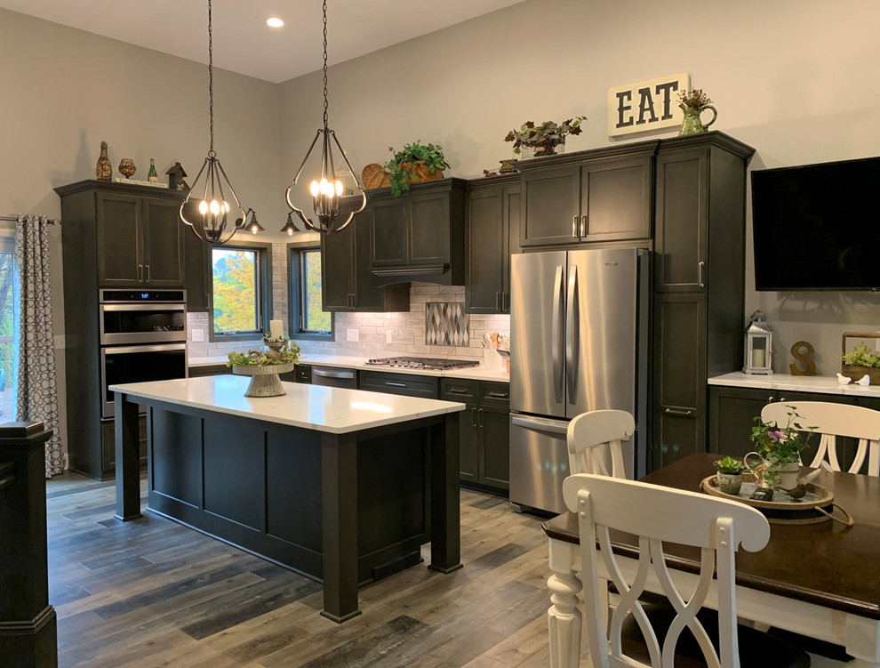 Inspiration for a large transitional u-shaped eat-in kitchen in Minneapolis with an undermount sink, shaker cabinets, quartz benchtops, white splashback, ceramic splashback, stainless steel appliances, with island, grey floor, white benchtop, black cabinets and medium hardwood floors.