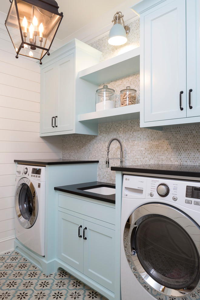 This is an example of a beach style single-wall dedicated laundry room in Minneapolis with shaker cabinets, blue cabinets, an undermount sink, white walls, multi-coloured floor and black benchtop.