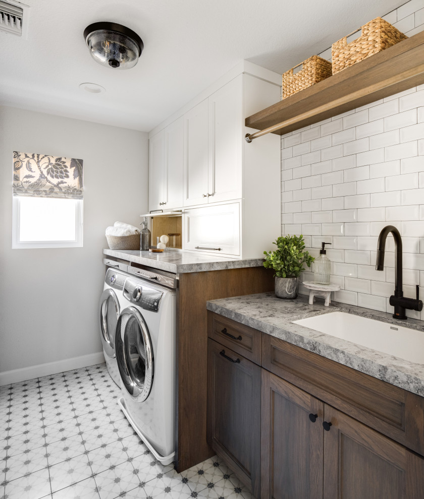 Photo of a mid-sized transitional galley dedicated laundry room in Orange County with an undermount sink, shaker cabinets, dark wood cabinets, quartz benchtops, white splashback, subway tile splashback, white walls, ceramic floors, a side-by-side washer and dryer, white floor and grey benchtop.