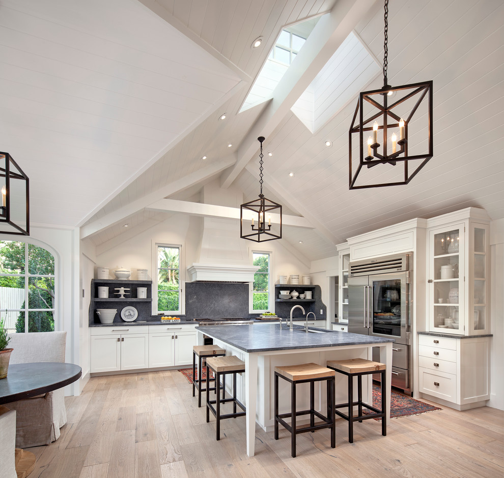 Photo of an expansive country l-shaped open plan kitchen in Santa Barbara with an undermount sink, shaker cabinets, white cabinets, light hardwood floors, with island, grey splashback, stone slab splashback and stainless steel appliances.